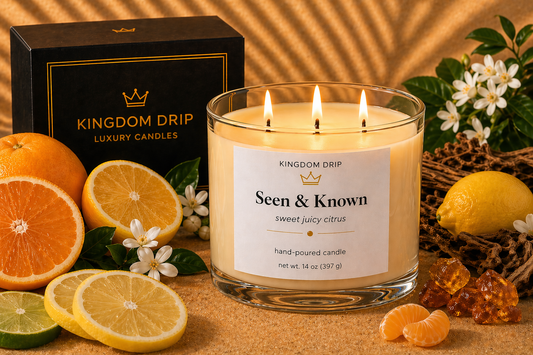 Kingdom Drip candle with 'Seen & Known' label surrounded by citrus fruits and flowers on a warm-toned background